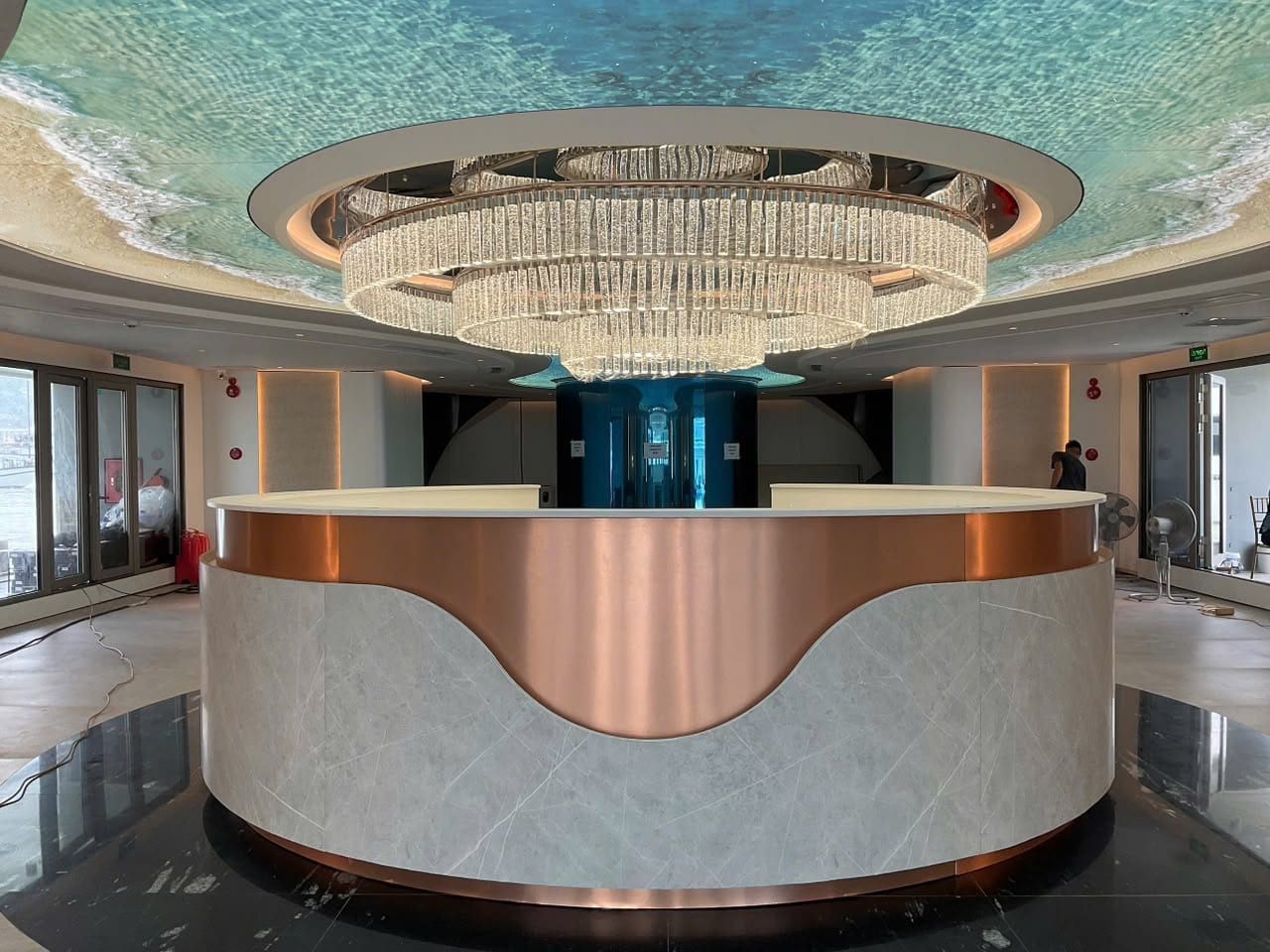 The reception lobby aboard Athena Premium, a tiered chandelier above a curved copper desk