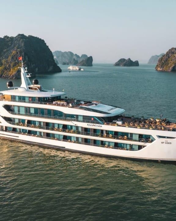 Azura Cruise at anchor below a forested limestone cliff